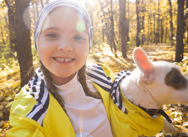 Campfire Circle A smiling little girl with pigtails in a yellow jacket holding a dog in her arms