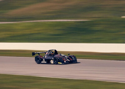 A wide shot of Team Earle’s #39 Radical SR3 XX, painted black, in motion during a race