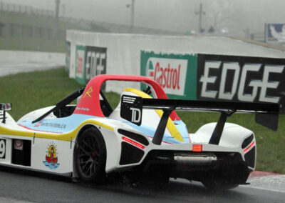 Team Earle’s #39 Radical SR3 XX, painted white, blue, and yellow, visible from the rear as it is about to make a turn on a race track