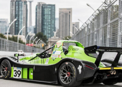 Team Earle’s #39 Radical SR3 XX, painted green and turning onto a Toronto street with skyscrapers in the background